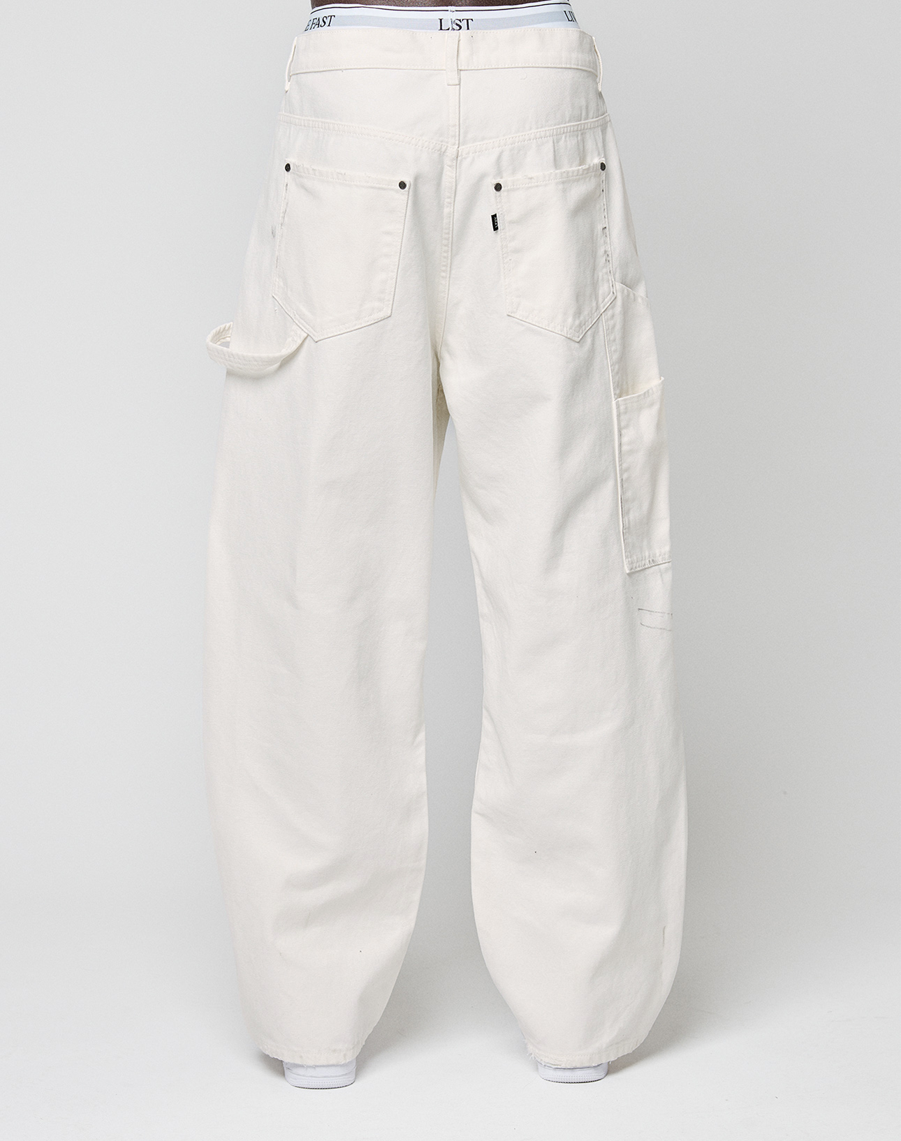 Back view of LIVE FAST DIE YOUNG Worker Pants in off-white, 100% cotton, with large back pockets, a carpenter pocket on the right leg, and a small loop on the left, shown against a plain white background.