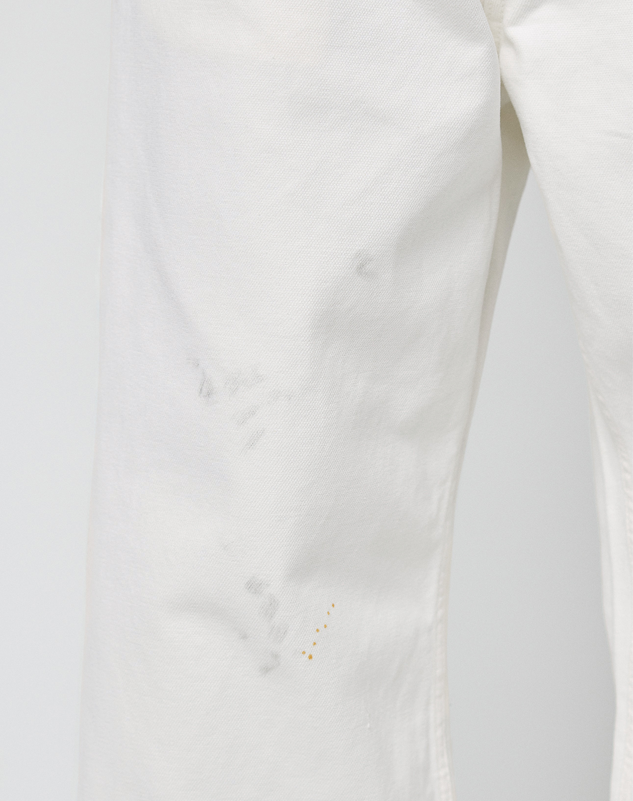 Close-up of LIVE FAST DIE YOUNG Worker Pants: baggy white style with faint gray smudges and small yellow stains on upper thigh and knee. Features a classic carpenter pocket design for extra functionality.
