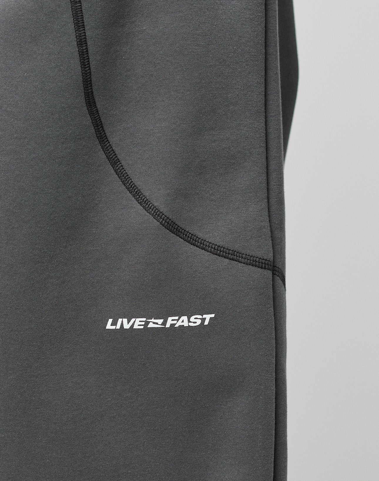 Close-up of the LFDY Active Fleece Jogger by LIVE FAST DIE YOUNG in dark gray, featuring black seams and a logo print with LIVE FAST and a dynamic graphic between the words.