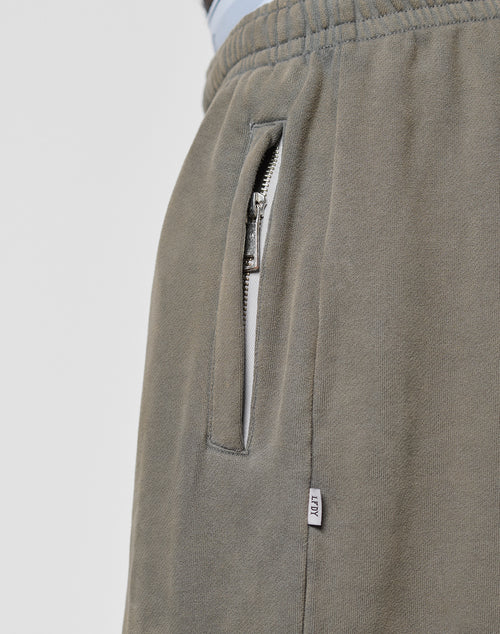 Close-up of LFDY Ripped Sweatpants by LIVE FAST DIE YOUNG in olive green, featuring a wide fit, elastic waistband, silver-zippered side pocket, and small white "NILI" tag. Made from 100% Baumwolle for comfort.