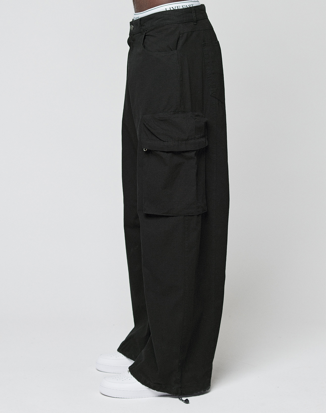 Someone wearing LIVE FAST DIE YOUNG’s LFDY Baggy Cargo pants with großen Cargo-Taschen and Baggy Fit, styled with white sneakers and posing against a plain white background.