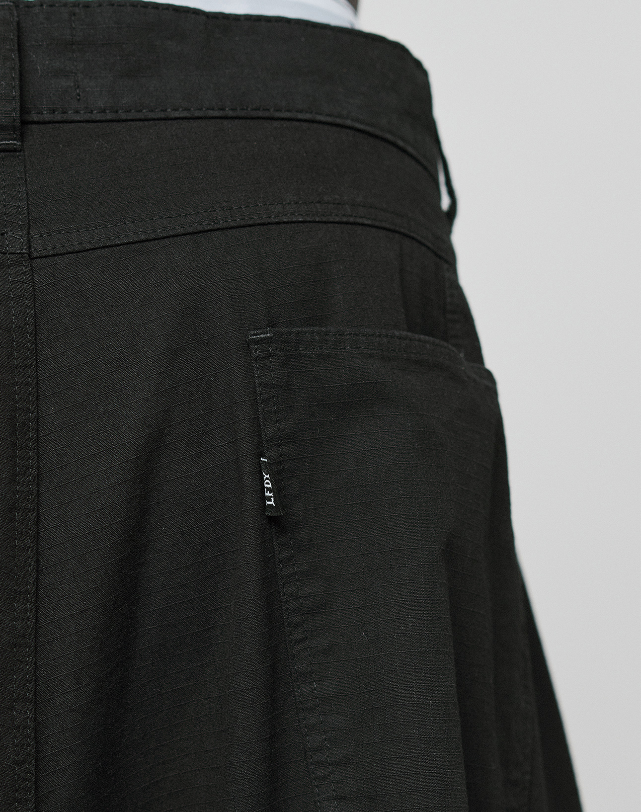 Close-up of the back of a person wearing LIVE FAST DIE YOUNG's LFDY Baggy Cargo pants, featuring a textured black fabric, back pocket with a small black tag, and partially visible waistband at the top.