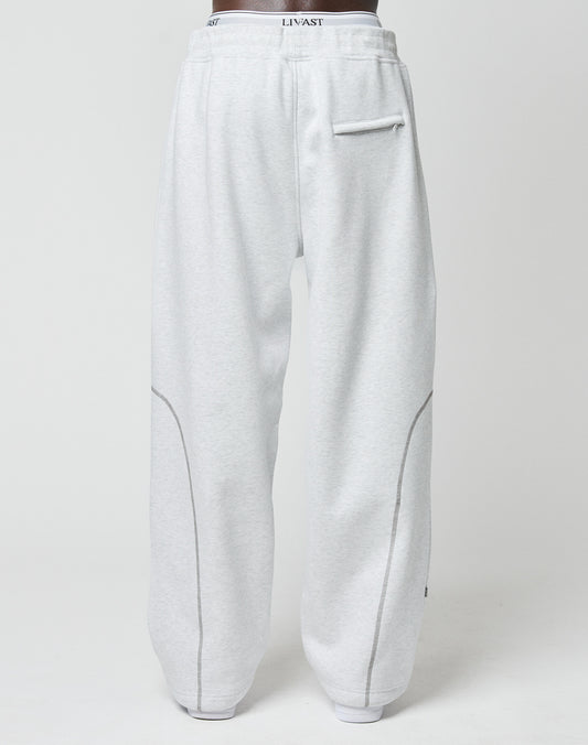 Someone is seen from behind in LFDY Active Fleece Joggers by LIVE FAST DIE YOUNG. These light gray pants have a wide fit, right-side back pocket, curved seams, and a waistband with LINVAST logo print.