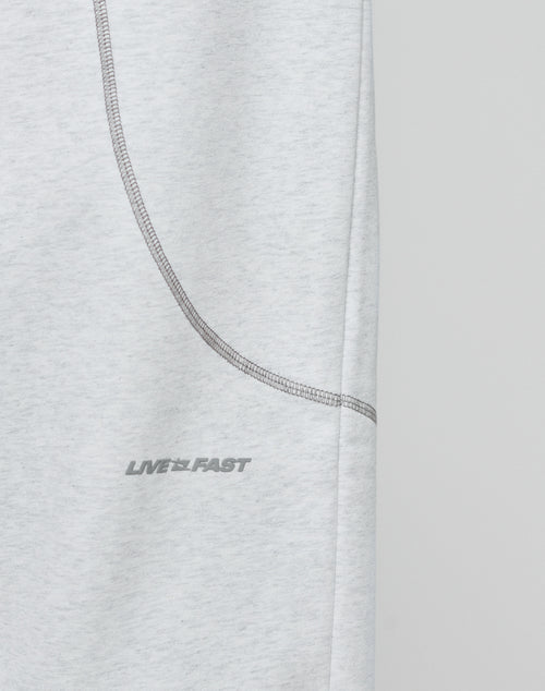 Close-up of the LFDY Active Fleece Jogger by LIVE FAST DIE YOUNG, featuring light gray fabric, a curved seam, and a subtle LIVE FAST logo in small gray uppercase letters. The background is plain and light-colored.