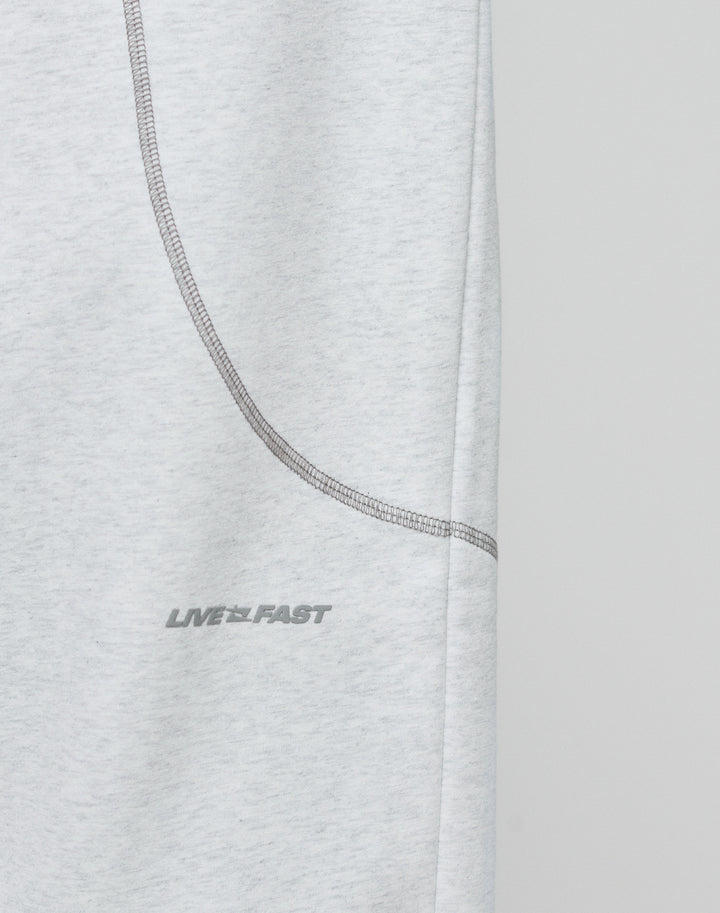 Close-up of the LFDY Active Fleece Jogger by LIVE FAST DIE YOUNG, featuring light gray fabric, a curved seam, and a subtle LIVE FAST logo in small gray uppercase letters. The background is plain and light-colored.