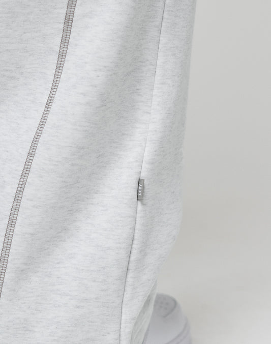 Close-up of LFDY Active Fleece Jogger by LIVE FAST DIE YOUNG in light gray, featuring a wide fit, visible side seam with contrast stitching, and a small branded fabric tag. The lower part of a white sneaker appears at the bottom.