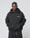 A person wears the LIVE FAST DIE YOUNG Basic 360 Hooded, a black oversized hoodie with white LiveFast chest print and topstitching, standing against a plain gray background and looking at the camera with hands in the front pocket.