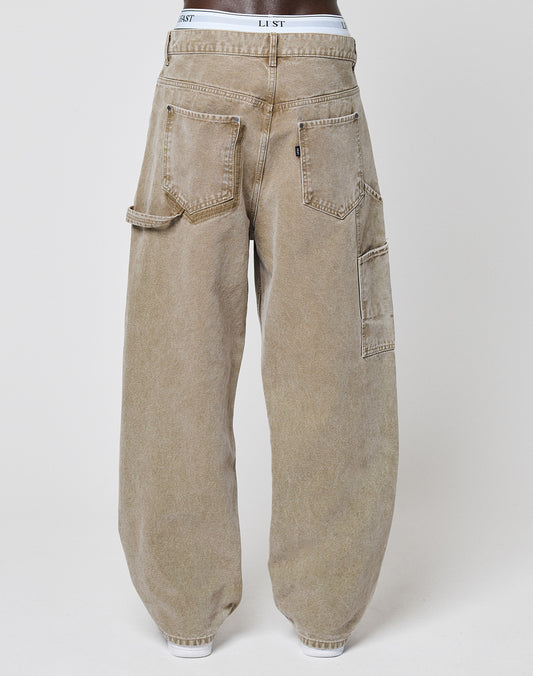 A person rocks the Carpenter Look in LIVE FAST DIE YOUNG Faded Carpenter Pants—baggy, light brown denim with large utility pockets. White LIST underwear peeks above the waist, adding a relaxed vintage vibe.