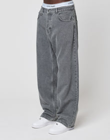 A person wearing LFDY Baggy Denim jeans by LIVE FAST DIE YOUNG, styled with white sneakers and visible white underwear featuring a LIVE FAST waistband, stands against a plain white background.