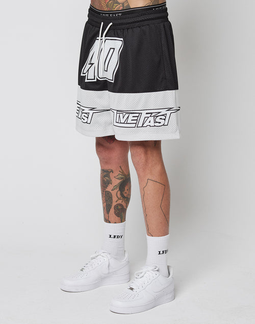 A person wearing LFDY Racing Mesh Shorts by LIVE FAST DIE YOUNG, featuring black and white mesh, number 40 and LIVE FAST print, paired with LFDY-branded white socks and white Nike sneakers, stands against a plain white background.