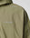 Close-up of the LIVE FAST DIE YOUNG Live Fast Trackjacket in light olive green with hood, regular fit, and white piping on shoulders. LIVE FAST is printed in white reflective text on the chest. Elastic cuffs provide a comfortable finish.
