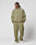 A person stands against a plain background wearing the LIVE FAST DIE YOUNG Live Fast Trackjacket in olive green with reflektierender Druck and white sneakers, hands in pockets and looking to the side.