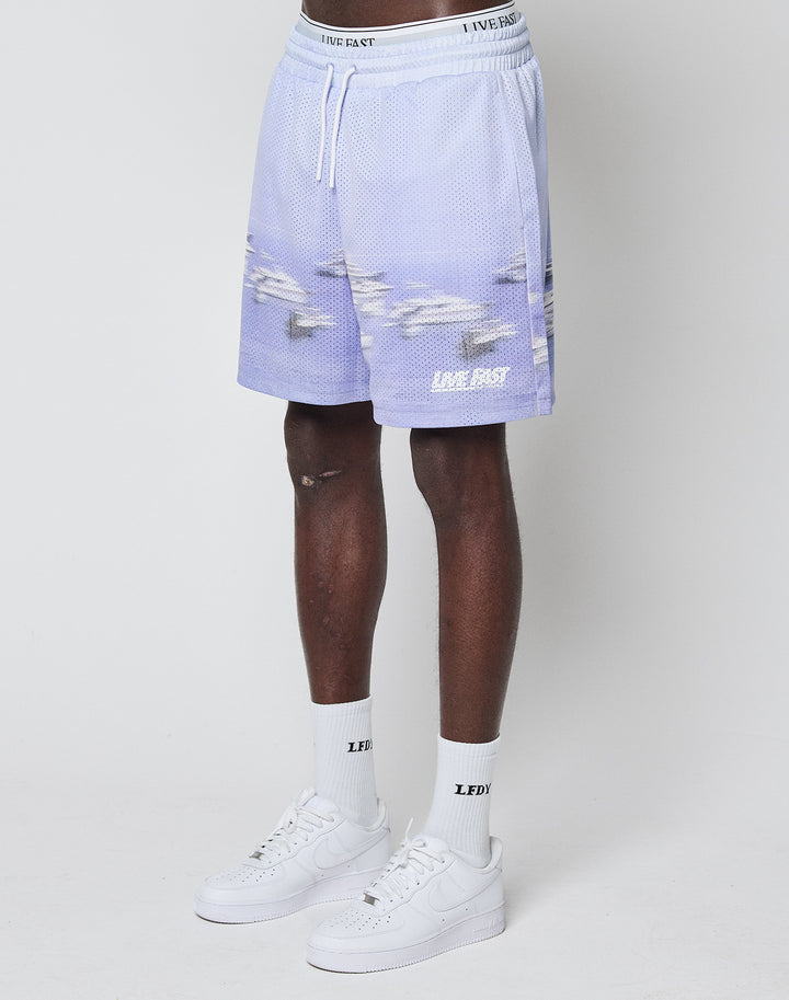 A person wears LIVE FAST DIE YOUNG LFDY Boat Mesh Shorts in light purple—regular fit, airplane and logo print, crafted from soft polyester—paired with white LFTY crew socks and white Nike sneakers, against a plain white background.