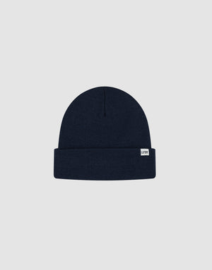 The Basic Beanie by LIVE FAST DIE YOUNG is a plain navy blue, one-size knitted hat with a folded brim and a white LFDT flaglabel on the front, made from soft polyacryl and shown on a light grey background.