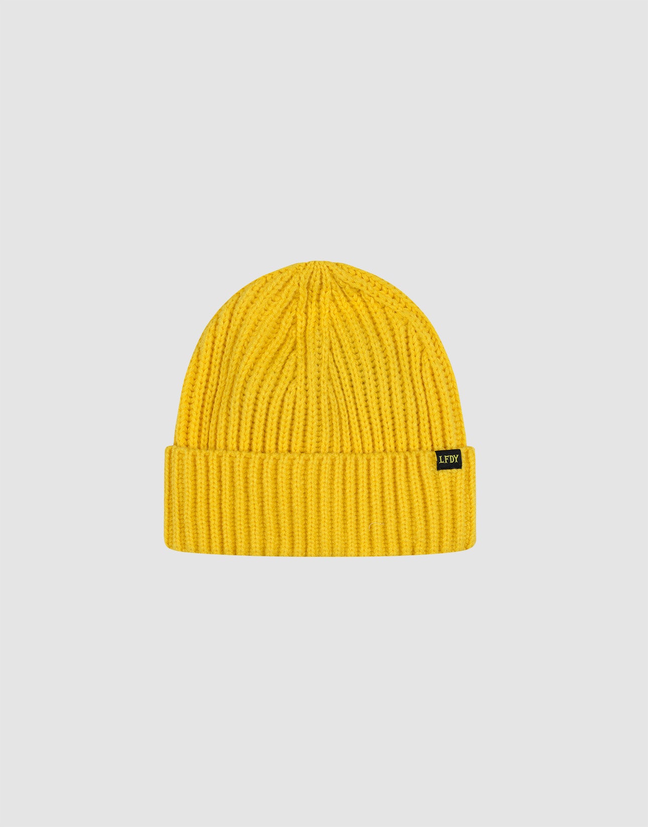 Die Rib Knit Beanie von LIVE FAST DIE YOUNG aus 100% Baumwolle zeigt sich im leuchtend gelben Rippenstrick mit umgeschlagenem Bund und kleinem schwarzen Label, präsentiert vor schlichtem hellgrauem Hintergrund.