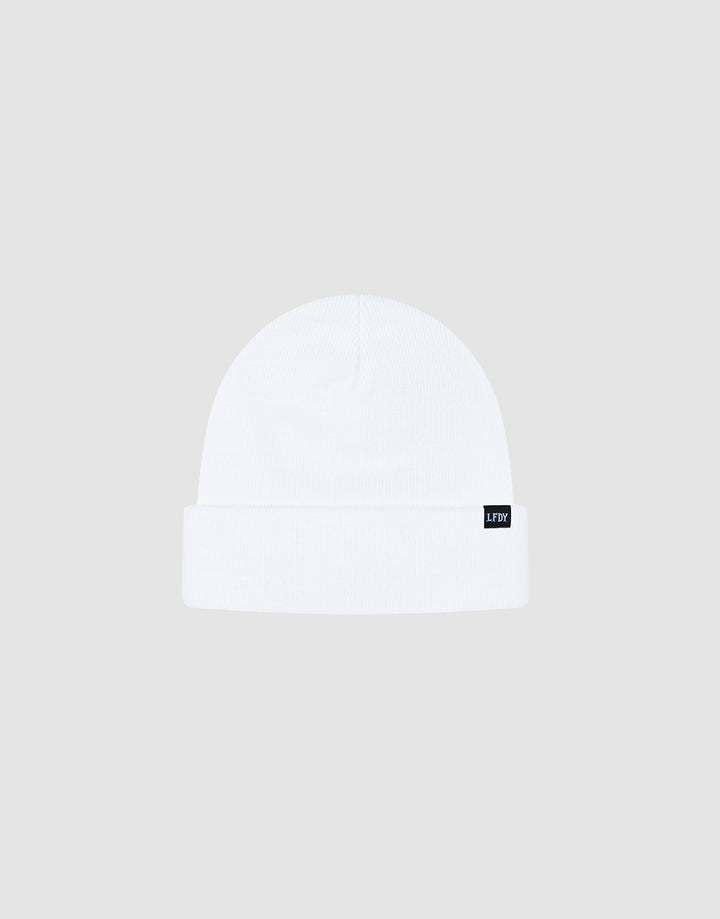 The Basic Beanie by LIVE FAST DIE YOUNG is a white polyacryl knit beanie with a folded brim and a black flag label on the side. It’s one size and shown against a light gray background.