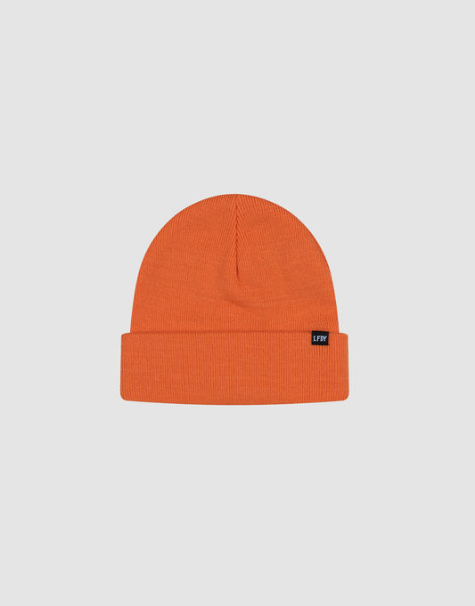 The LIVE FAST DIE YOUNG Basic Beanie is an orange Polyacryl knit hat with a folded brim and small black flaglabel on the side, shown on a light gray background. This one size beanie combines style and comfort for any occasion.