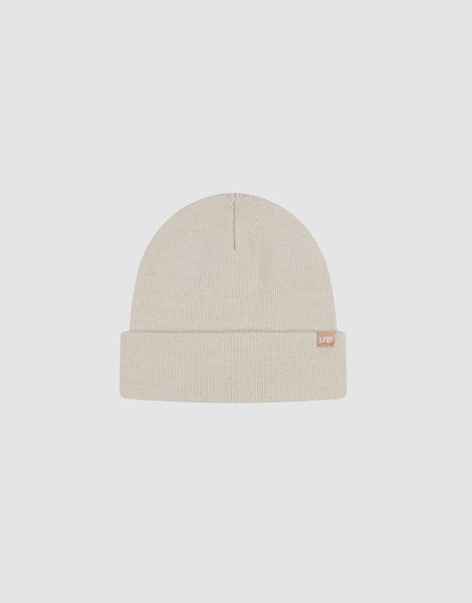 The LIVE FAST DIE YOUNG Basic Beanie is a beige polyacryl knit hat with a folded brim and a small flaglabel tag on the edge, shown against a plain light gray background.