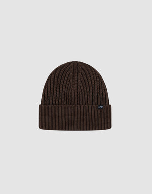A dark brown Rib Knit Beanie by LIVE FAST DIE YOUNG in polyacryl with a folded cuff, shown on a light gray background. Features a small black tag with white text on the cuff. One Size for versatile wear.