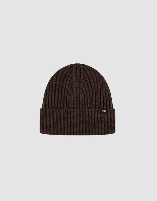 A dark brown Rib Knit Beanie by LIVE FAST DIE YOUNG in polyacryl with a folded cuff, shown on a light gray background. Features a small black tag with white text on the cuff. One Size for versatile wear.