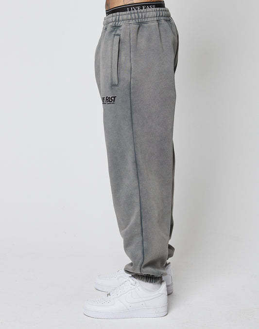 A person wears the LFDY Europe Run Jogger by LIVE FAST DIE YOUNG, featuring a vintage wash, elastic waistband with LIVE FAST text, side pockets, and white sneakers. Side view photo against a plain white background.