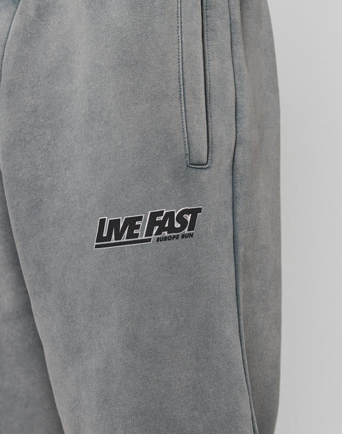 Close-up of LFDY Europe Run Jogger by LIVE FAST DIE YOUNG. Grey, loose fit sweatpants with side pockets, elastic cuffs, and LIVE FAST EUROPE RUN printed in black and white on the upper thigh.