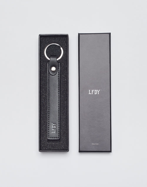 The LIVE FAST DIE YOUNG Basic Keychain, made of black PU leather with silver hardware and an embossed LFDY logo, is shown in a foam-padded black box. A closed black box with LFDY on the lid sits beside it.