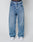 A person in LFDY Baggy Denim by LIVE FAST DIE YOUNG, blue jeans with a wide straight leg made from 100% cotton, pairs the look with white sneakers. The LIVE FAST waistband of dark underwear is visible above the jeans against a plain white background.