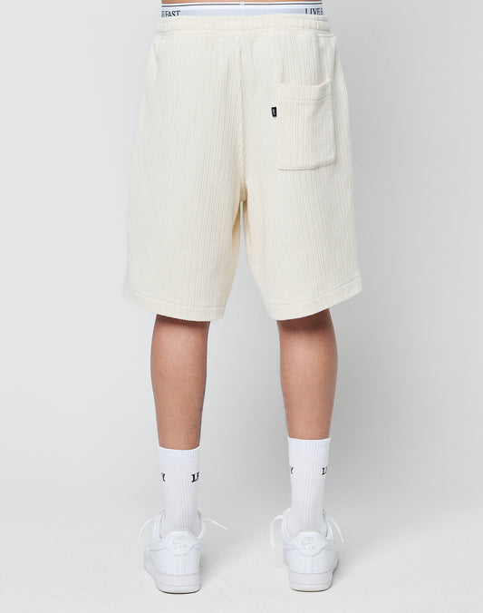 A person is shown from the back wearing off-white LIVE FAST DIE YOUNG Basic Knit Shorts with a back pocket, white crew socks, and white sneakers against a plain light background.