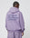 A person with braided hair wears an oversize fit, loose lavender Basic 360 Hooded and matching pants by LIVE FAST DIE YOUNG. Bold LiveFast HvySweat 360g/m² text, plus smaller details, appear on the back. Made from premium cotton-polyester.