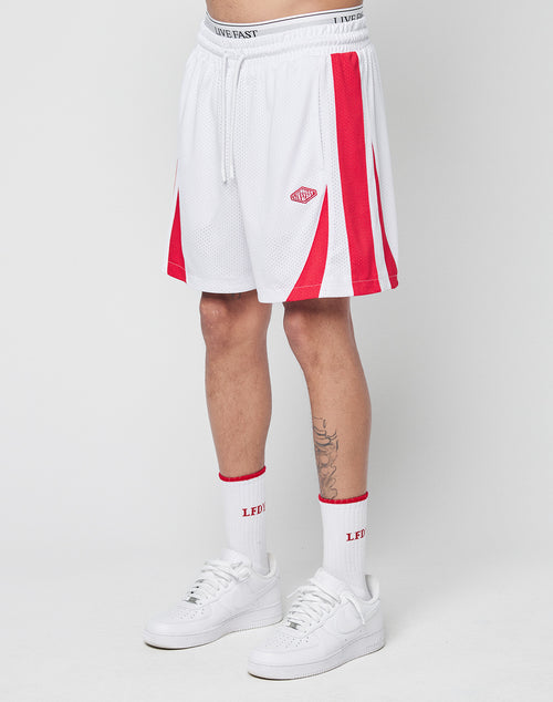 A person wears LIVE FAST DIE YOUNG Striped Mesh Shorts with a white waistband, red accents, a logo patch, white crew socks featuring red LEDI text, and white sneakers, standing against a plain white background.