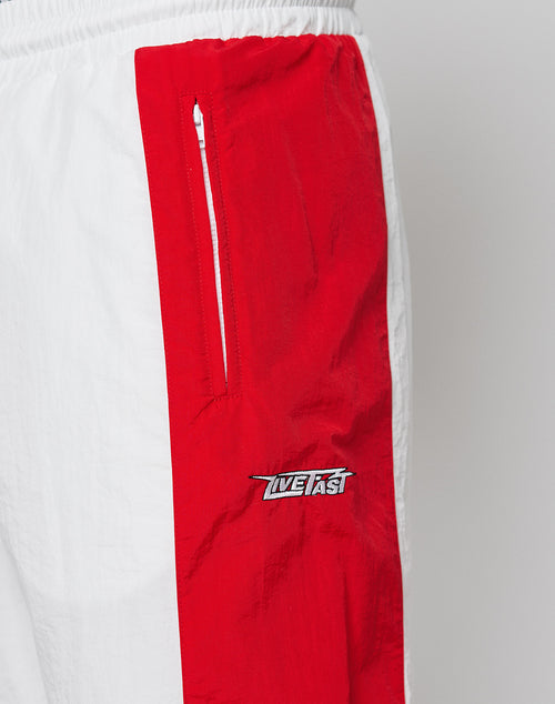 Close-up of LFDY Trackpants 3000 by LIVE FAST DIE YOUNG: wide fit white pants with a bold red side stripe, zippered pocket, elastic waistband, and “Live Fast” embroidered on durable polyamide.