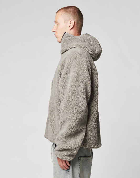 A person with short hair stands in profile against a light background, wearing an oversize fit LIVE FAST DIE YOUNG Live Fast Teddy Jacket with embossed branding and light-wash jeans.