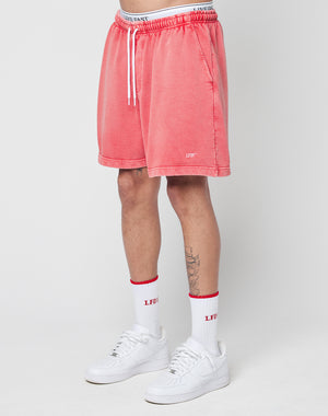 A person wears LIVE FAST DIE YOUNG Basic Sweat Shorts in coral pink with a handmade fade effect, white crew socks with red accents, and white sneakers. Only the lower half of the body is shown against a plain white background.