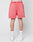 A person faces away, wearing LIVE FAST DIE YOUNG Basic Sweat Shorts in coral pink with elastic waistband and handmade fade effect, plus white socks with red trim and white sneakers, set against a plain light background.
