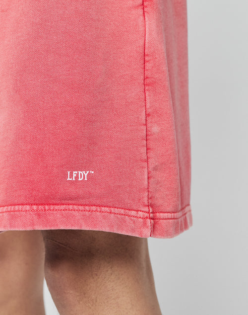 A close-up of a person wearing LIVE FAST DIE YOUNG Basic Sweat Shorts in pink, featuring an elastic waistband and a white LFDY™ logo near the hem. Only part of the leg and the subtly faded lower shorts are visible.