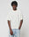 A person with short, curly hair stands against a plain background, wearing the LIVE FAST DIE YOUNG LFDY Flash Tee—an off-white oversize fit T-shirt with a small red logo on the chest—and light blue ripped jeans. One hand is in their pocket.