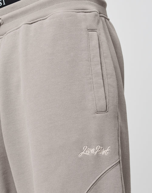 Close-up of Basic Wide Jogger sweatpants in light taupe by LIVE FAST DIE YOUNG, featuring an elastic waistband, side pocket, and Live Fast embroidered in white on the upper thigh. Made from soft cotton for comfort and style.