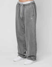 A person wearing LIVE FAST DIE YOUNG Basic Wide Jogger sweatpants in gray with a left thigh logo, wide fit, and white sneakers stands against a plain white background. | model