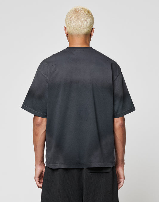 A person with short, bleached blond hair is seen from the back, wearing a dark oversize LFDY Flames Tee by LIVE FAST DIE YOUNG and black shorts against a plain light background.