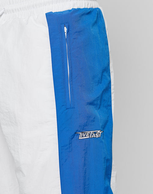 Close-up of LFDY Trackpants 3000 by LIVE FAST DIE YOUNG featuring white and blue color blocking, a vertical zippered pocket, INFAST logo on blue fabric, comfortable elastikbund, wide fit for a relaxed look, and wrinkled texture.