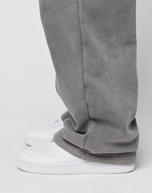 Someone stands against a plain light background wearing LIVE FAST DIE YOUNGs Basic Wide Joggerāloose-fitting gray pants with an elastic waistband and drawstringāthat cover the tops of white sneakers.