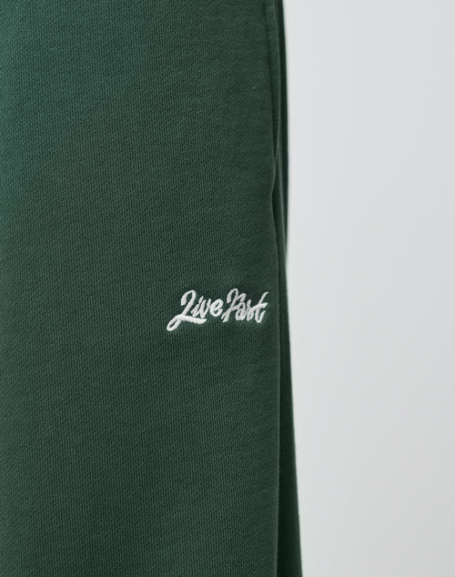 The Basic Wide Jogger by LIVE FAST DIE YOUNG features dark green Baumwolle fabric with Live Fast embroidered in white cursive. The wide fit and textured material stand out against a plain, out-of-focus background.