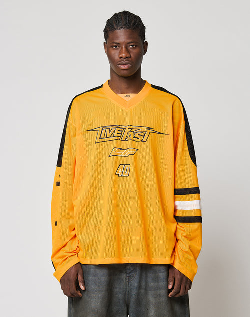 A person with braided hair wears the LFDY Autobahn Jersey by LIVE FAST DIE YOUNG—an oversize yellow polyester jersey featuring black and white sleeve stripes, the number 40, multilogo accents, and LIVE FAST on the front—against a light background.