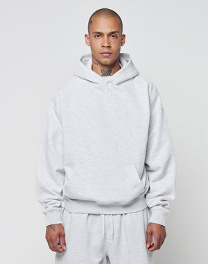 A person with a shaved head models the LIVE FAST DIE YOUNG Basic Blank Hooded and matching sweatpants in light gray, featuring an oversize fit and soft Baumwolle fabric, standing forward against a plain background.