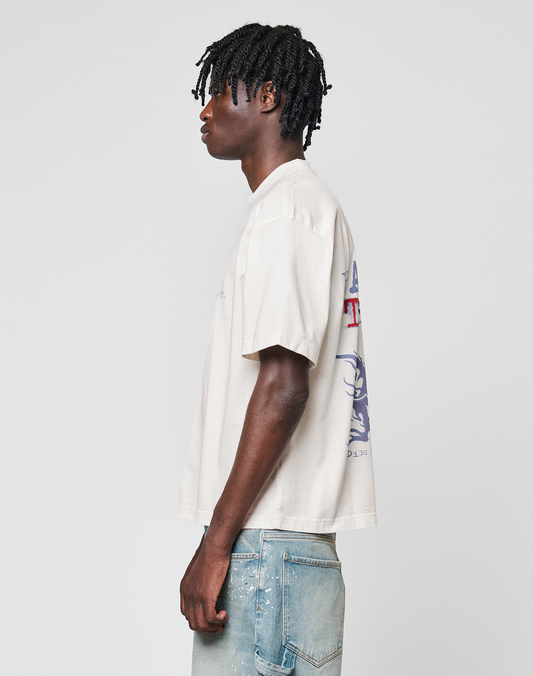 A person with short, twisted hair stands in profile against a plain background, wearing the LFDY We Walked Tee by LIVE FAST DIE YOUNG in an oversize fit with front and back prints, paired with light blue jeans with visible stitching.