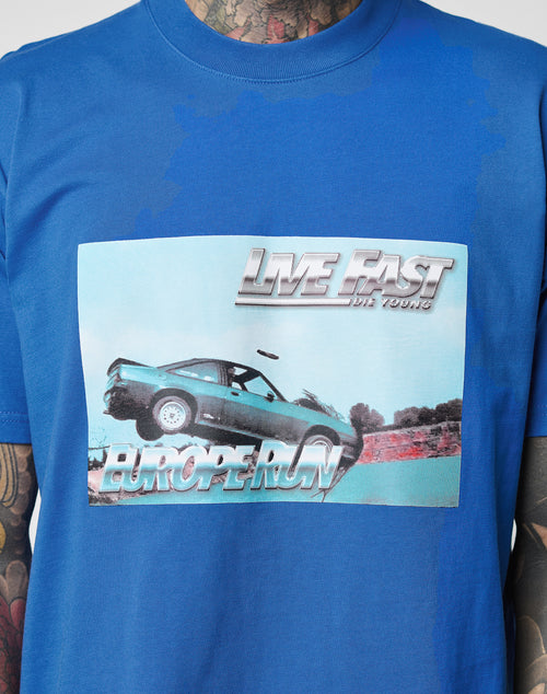 The LFDY Crash Kid Tee by LIVE FAST DIE YOUNG is a blue Baumwolle t-shirt featuring a car graphic, “LIVE FAST DIE YOUNG” at the top and “EUROPE RUN” at the bottom, plus topstitching am Halsloch. Wearer’s tattooed neck and arms partly visible.