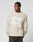A man in the LIVE FAST DIE YOUNG Live Fast Fuzzy Sweater, featuring a bold intarsia logo, polyamid-elastan mix, oversize fit, and light beige color, stands against a plain background looking to his left.
