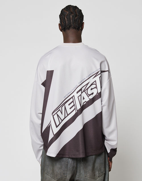 Seen from behind against a plain white background, a person with braided hair wears the LFDY Racetrack Jersey by LIVE FAST DIE YOUNG—an oversized, long-sleeve shirt with a bold diagonal design and LIVE FAST printed large on the back.
