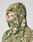 A person wears the LIVE FAST DIE YOUNG Live Fast Teddy Jacket in beige and green camo, featuring a hood with visor opening that reveals part of their face. Subtle embossed branding accents the fleece, set against a light gray background.